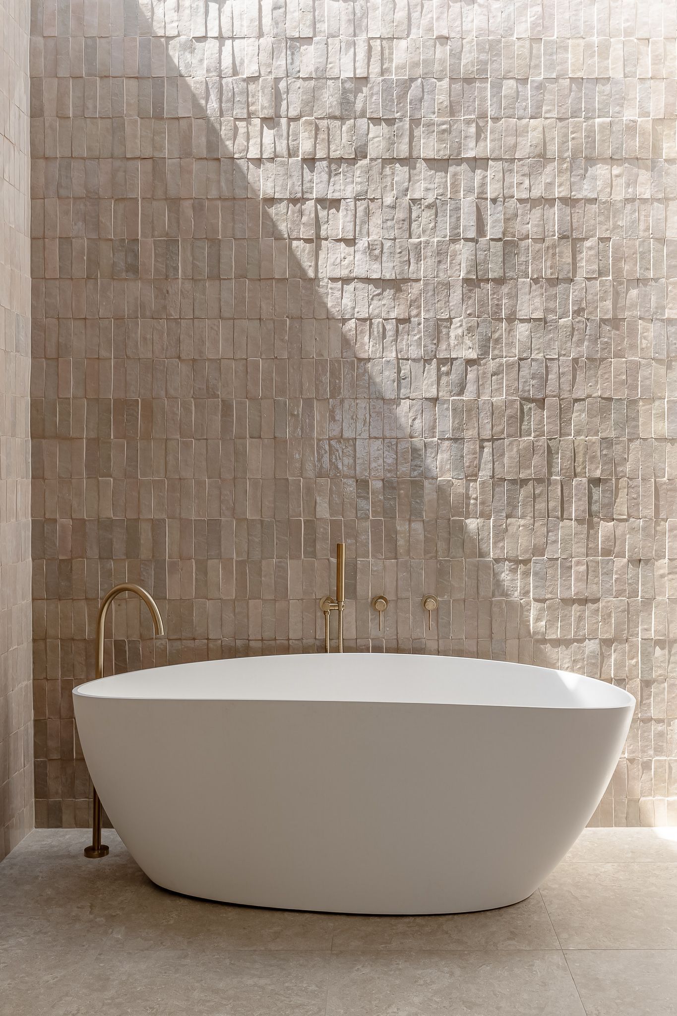 Freestanding White Bathtub With Gold Fixtures Against Textured Beige Wall — SDC Building Design In Kiama, NSW