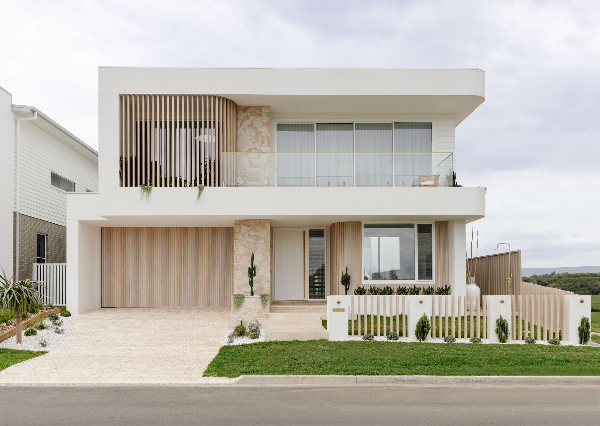 Modern two-story white house with wooden accents and slatted facade, gravel driveway, and a small green yard — SDC Building Design In Kiama, NSW