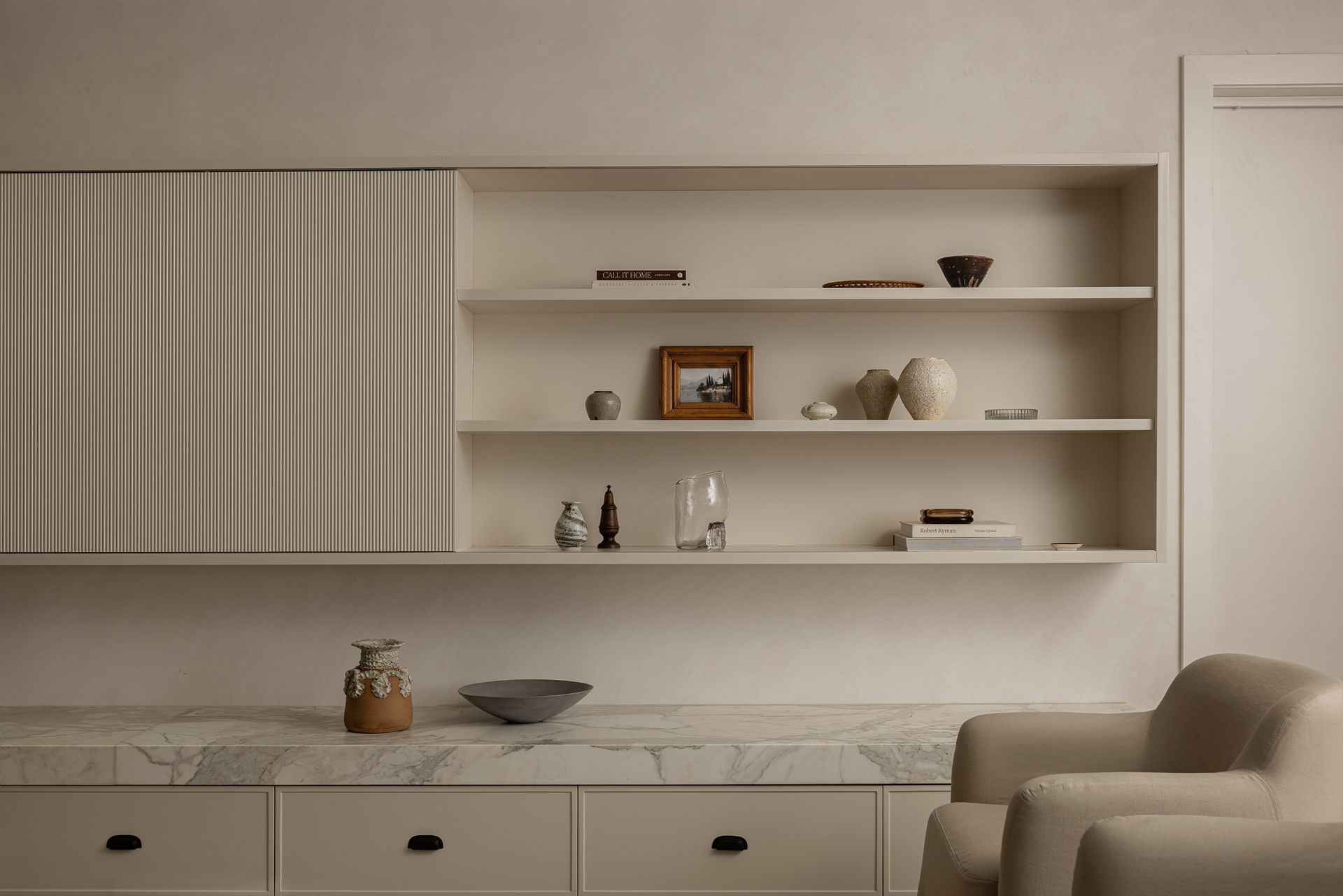 Built-in shelving with decorative items, next to a cabinet with textured paneling, above a marble countertop — SDC Building Design In Kiama, NSW
