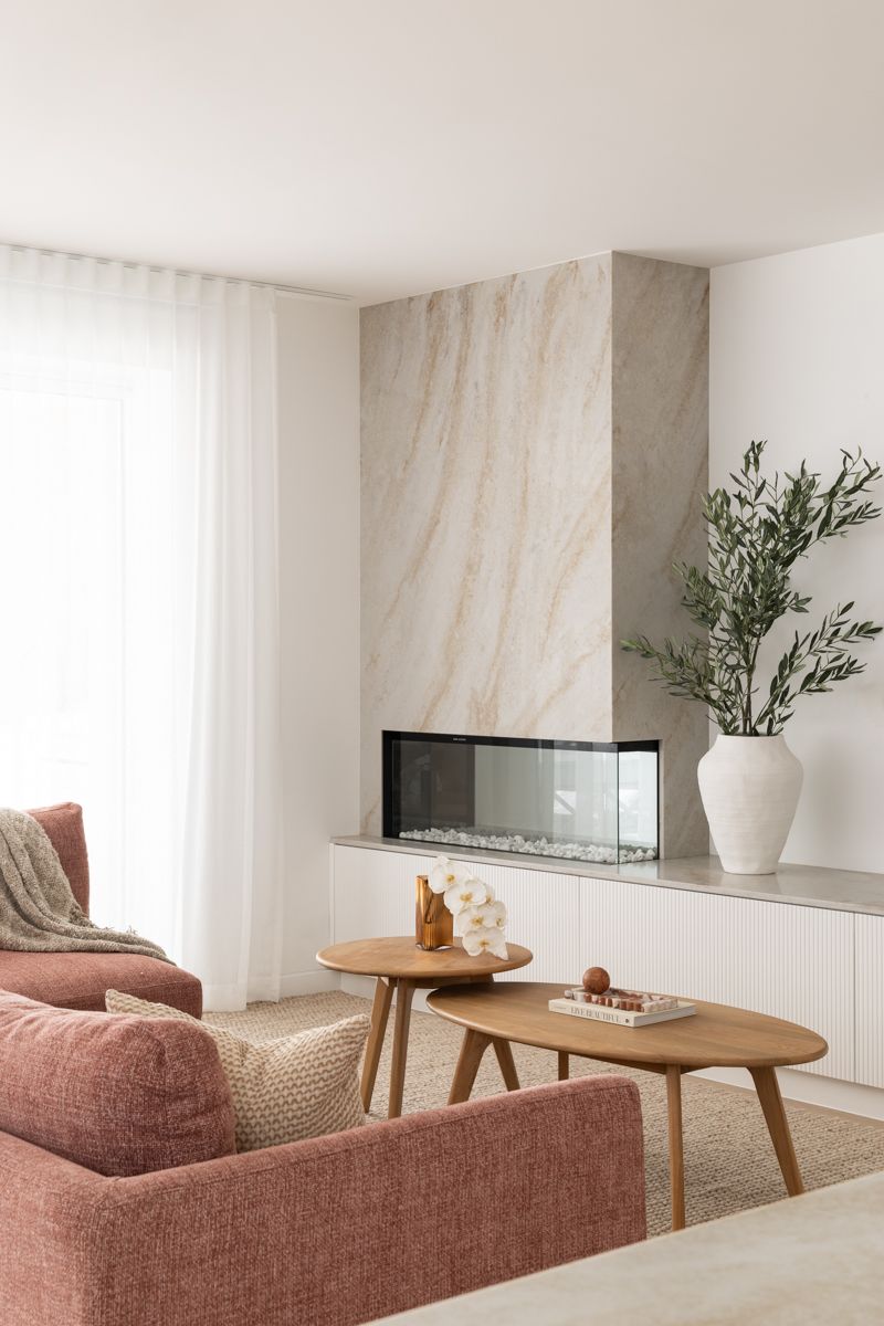 Living room with a fireplace, pink sofa, and wooden coffee tables. — SDC Building Design In Kiama, NSW