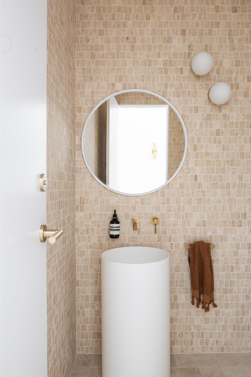 Bathroom with beige mosaic tile walls, white pedestal sink, round mirror, and brass fixtures. — SDC Building Design In Kiama, NSW