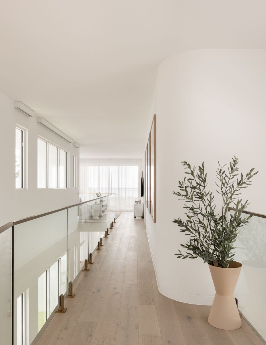 Bright, modern hallway with glass railing, light wood floors, and potted plant. — SDC Building Design In Kiama, NSW