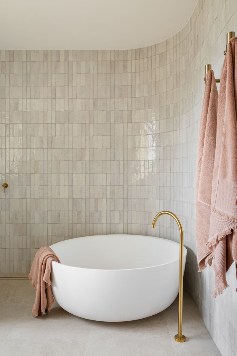 A white, round bathtub in a bathroom with light gray tiled walls and pink towels. — SDC Building Design In Kiama, NSW