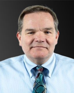 man with brown hair wearing a blue shirt with a colored tie