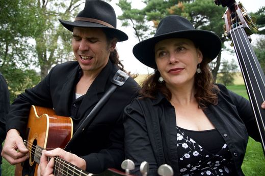 Two musicians in hats play guitar and stand-up bass outdoors.