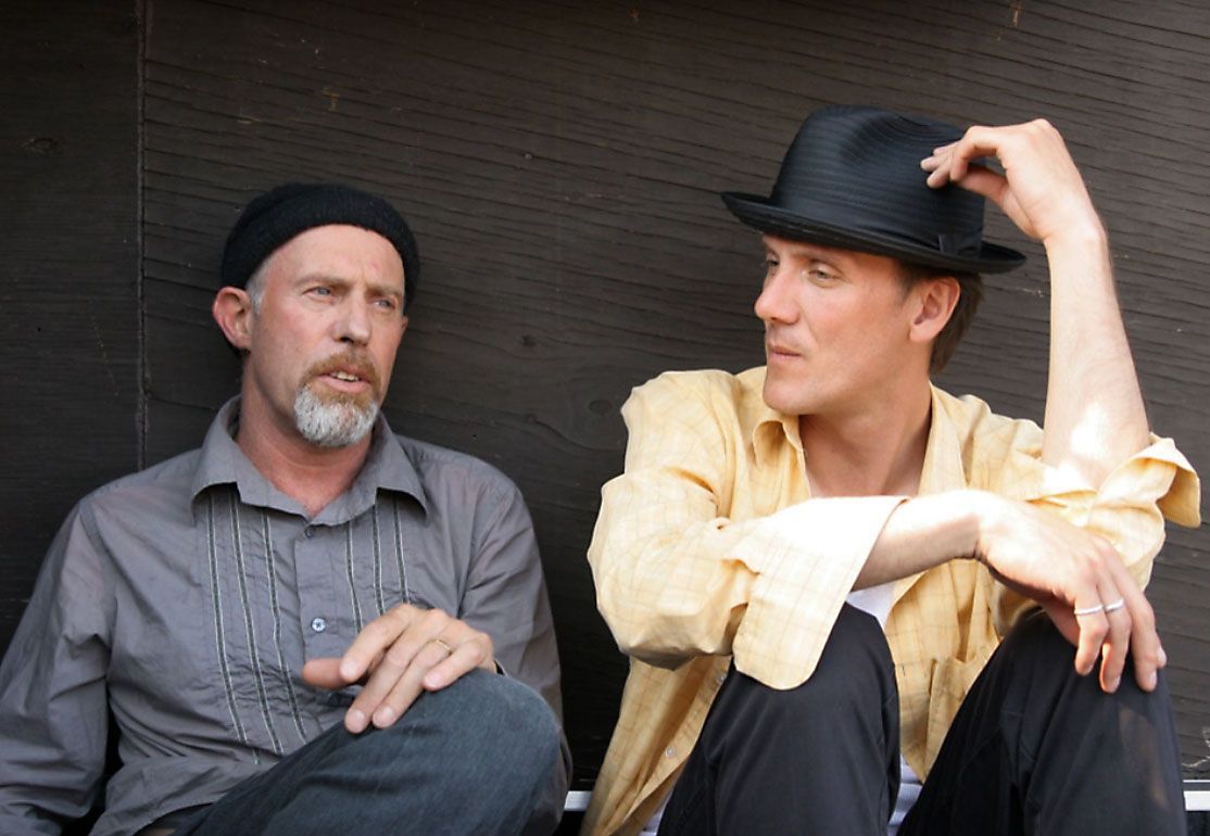 Two men sitting next to each other one wearing a hat