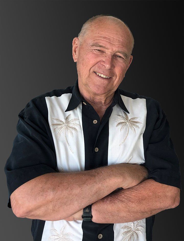 A man in a black and white shirt is standing with his arms crossed and smiling.