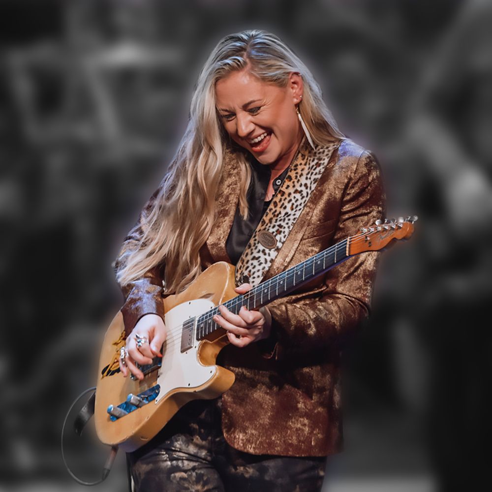 A woman in a leopard print jacket is playing a guitar.
