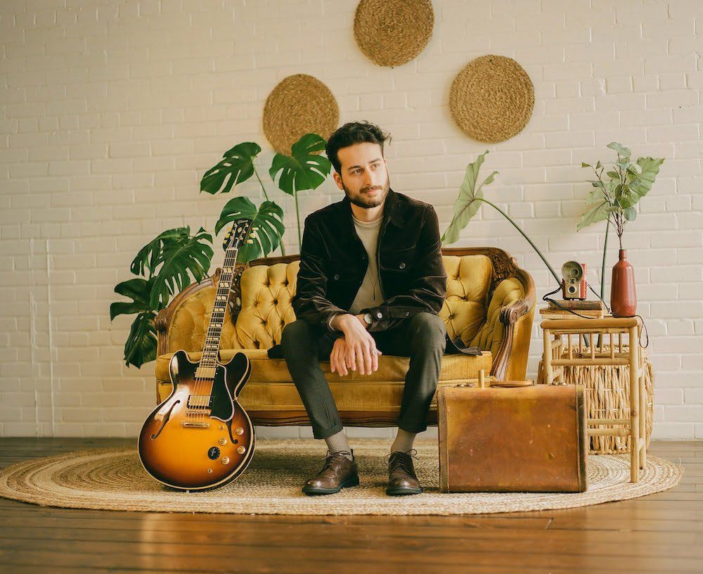 A man is sitting on a couch with a guitar next to him.
