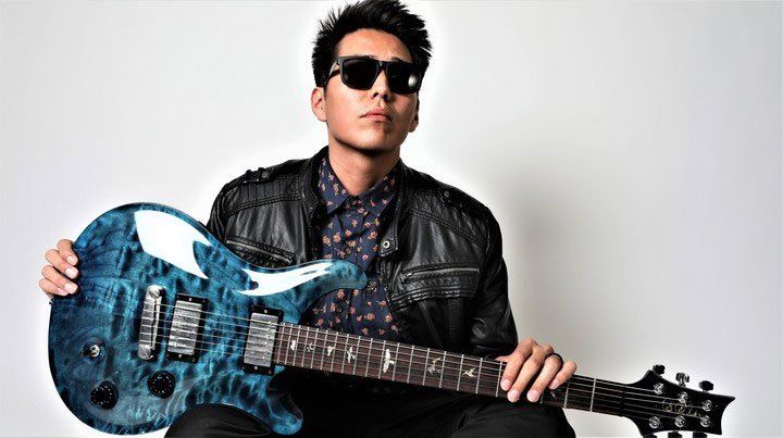 A man wearing sunglasses is holding a blue electric guitar.