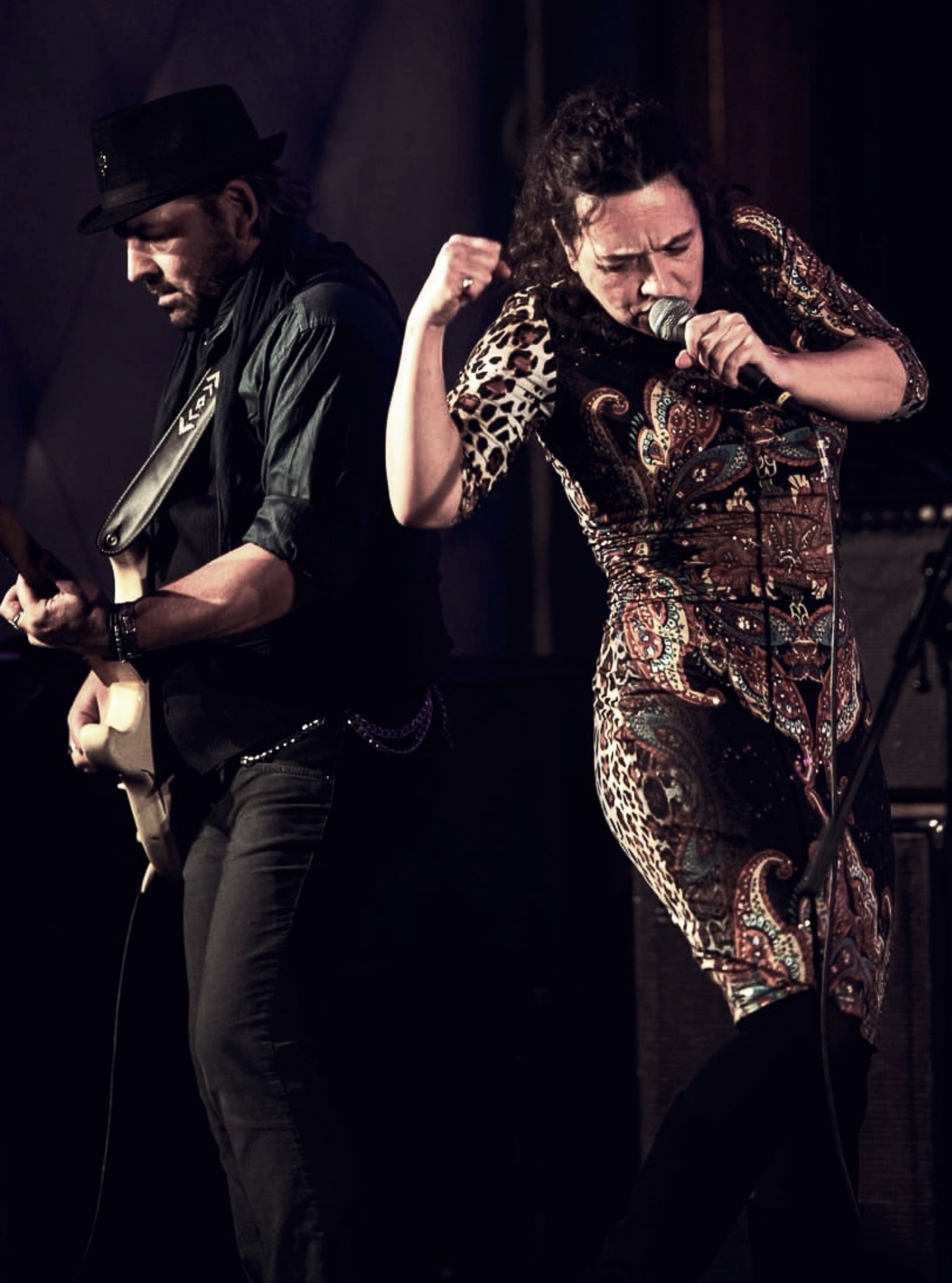 A man with hat on playing guitar as woman with guitar sits beside with a guitar in hands