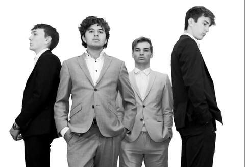 Four young men in suits, standing together against a white background.