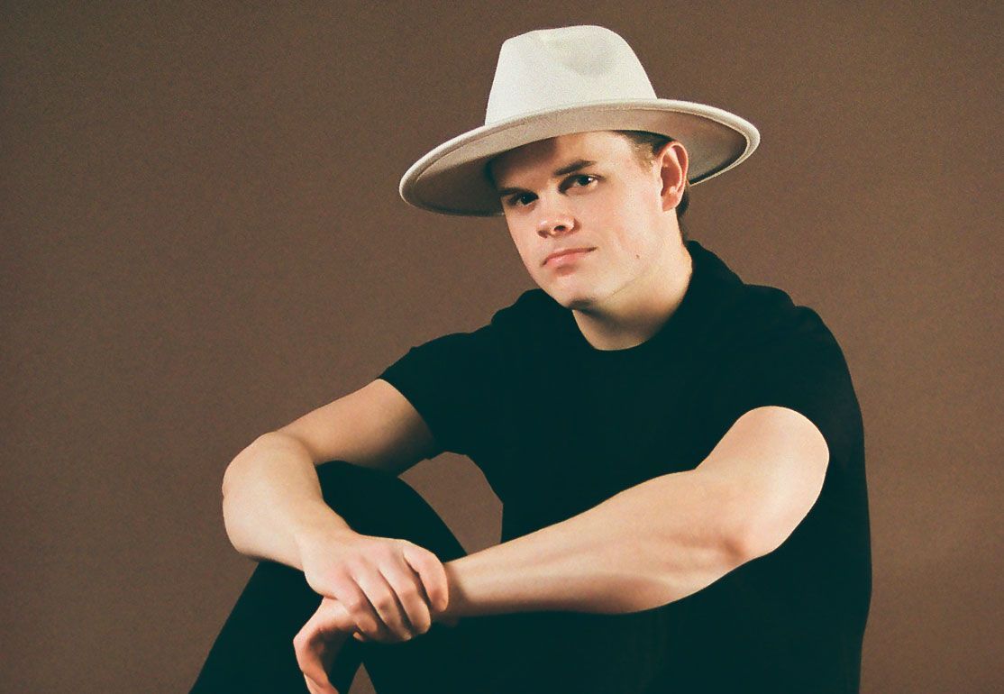 A young man wearing a white hat and a black shirt is sitting down.