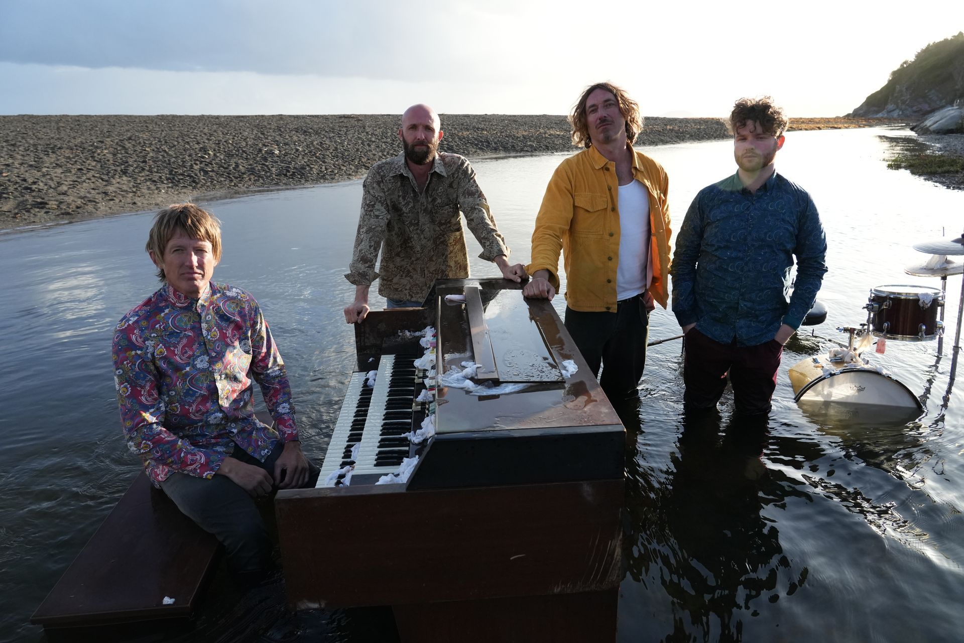 Three people posing in front of a graffiti wall. All wear sunglasses. The person in the center wears a hat and pink jacket.
