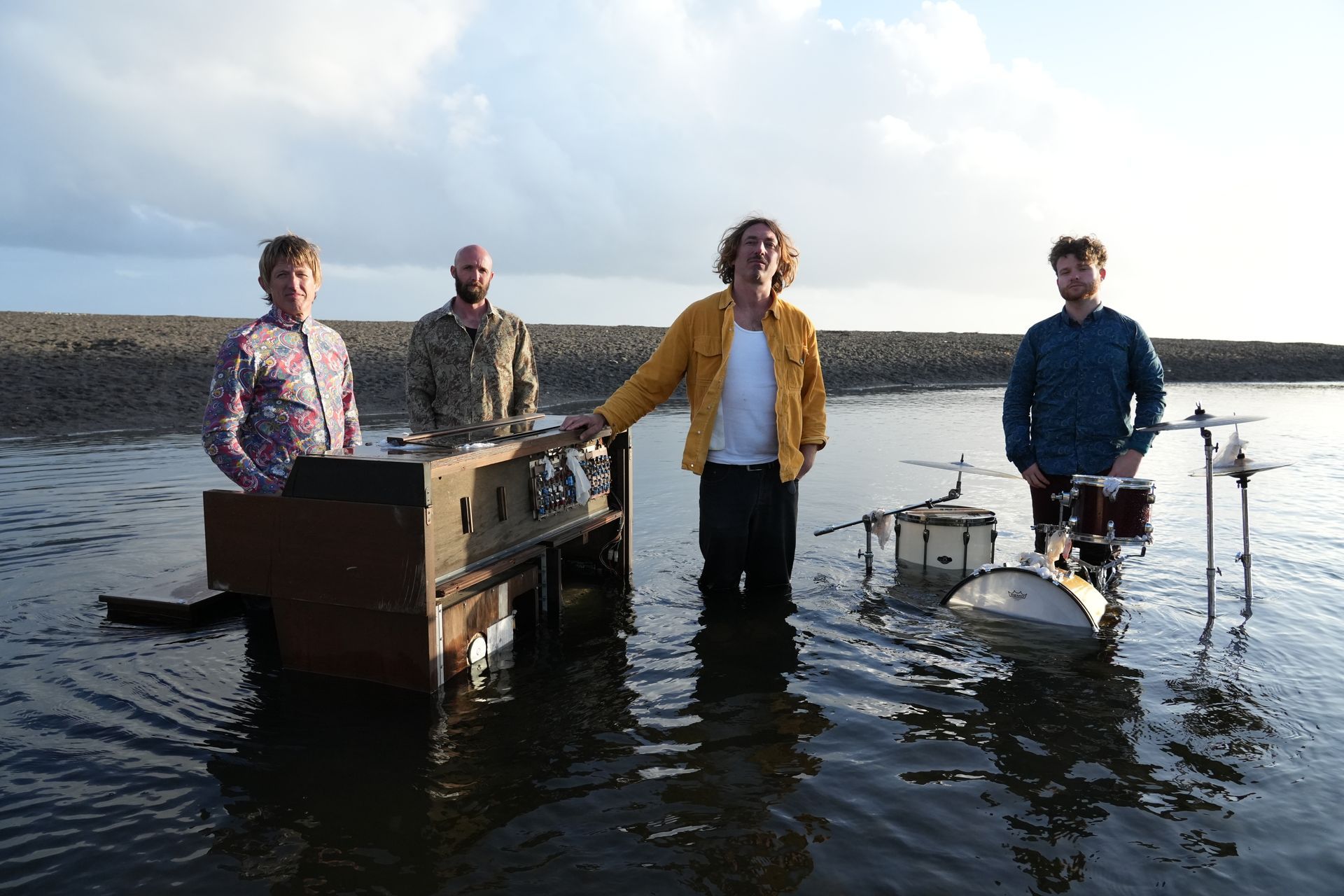 Five member of band standing beside drums and piano sitting in body water
