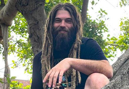 A man with dreadlocks and a beard is sitting in a tree.