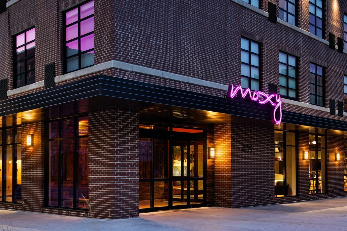 A brick building with a neon sign that says ' Moxy ' on it