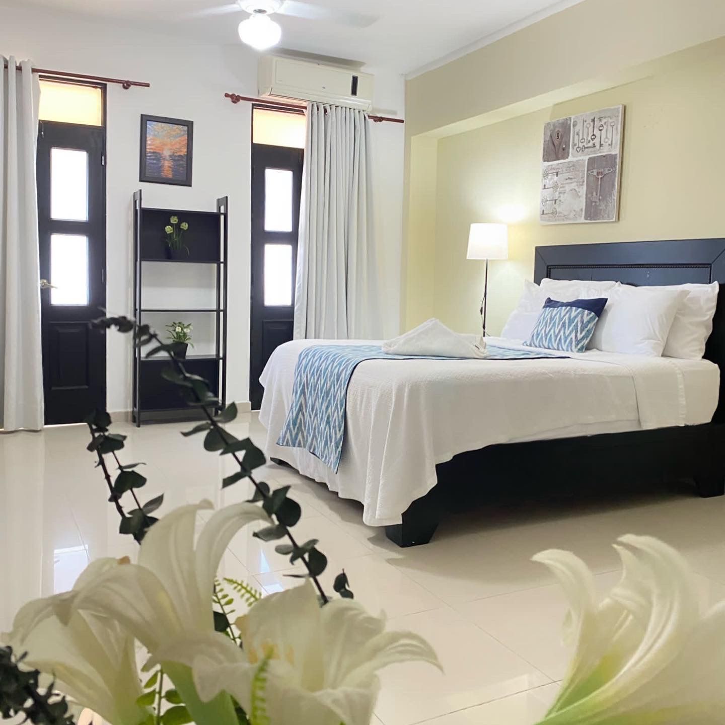 Bedroom with a bed, artwork, and decorative flowers. Black doors and white curtains.