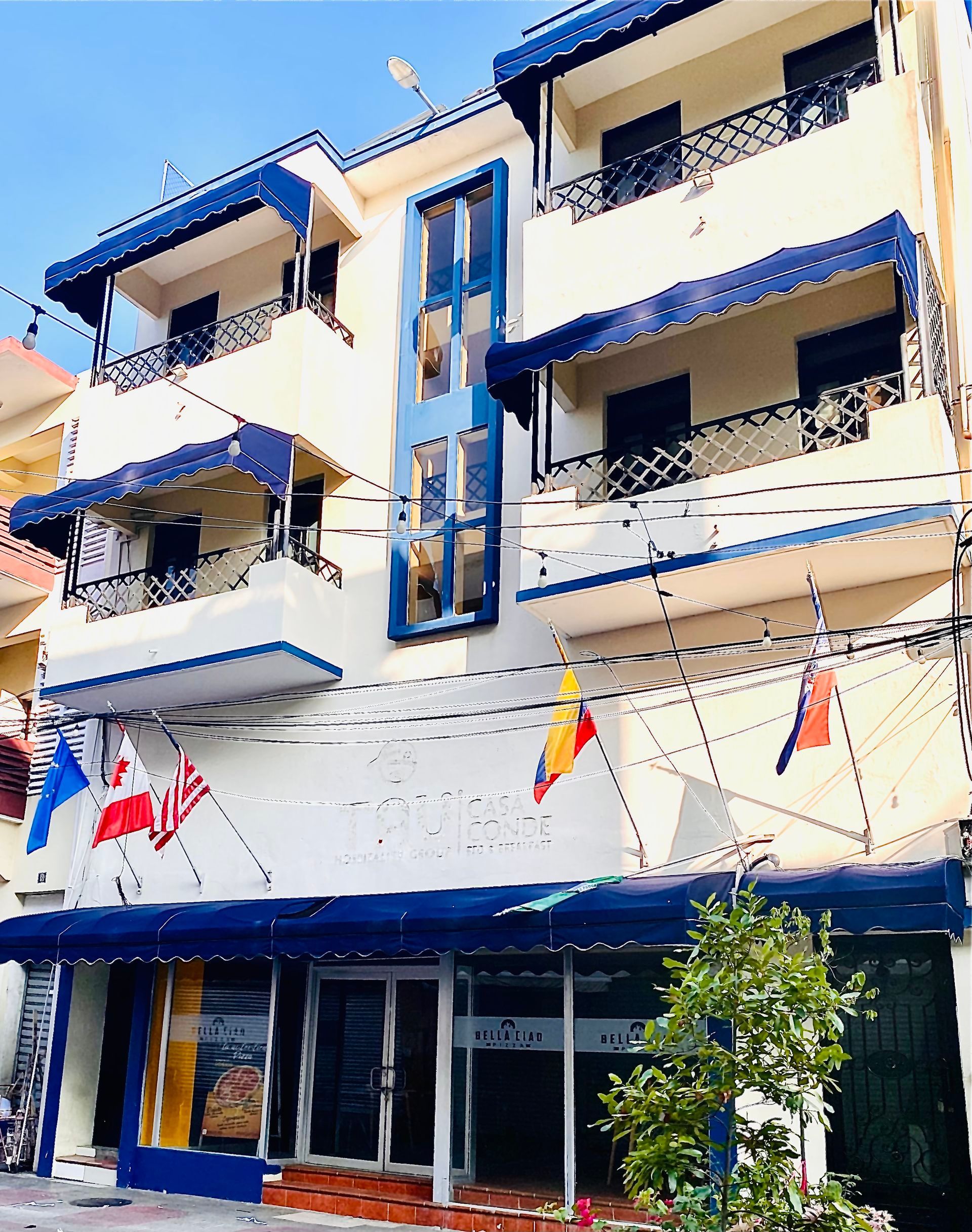 Three-story building with blue accents, awnings, and flags; storefront at the bottom.
