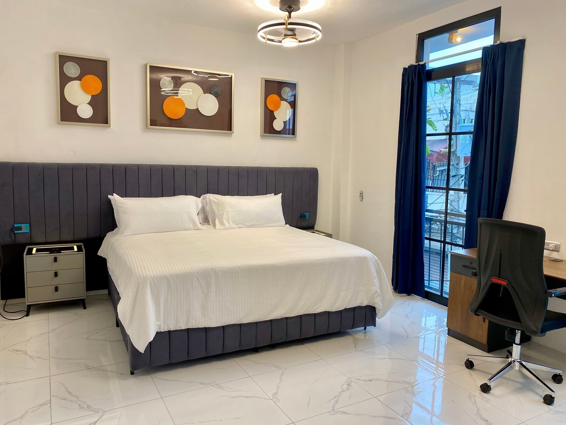 Bedroom with king-sized bed, art, desk, and large window with blue curtains.