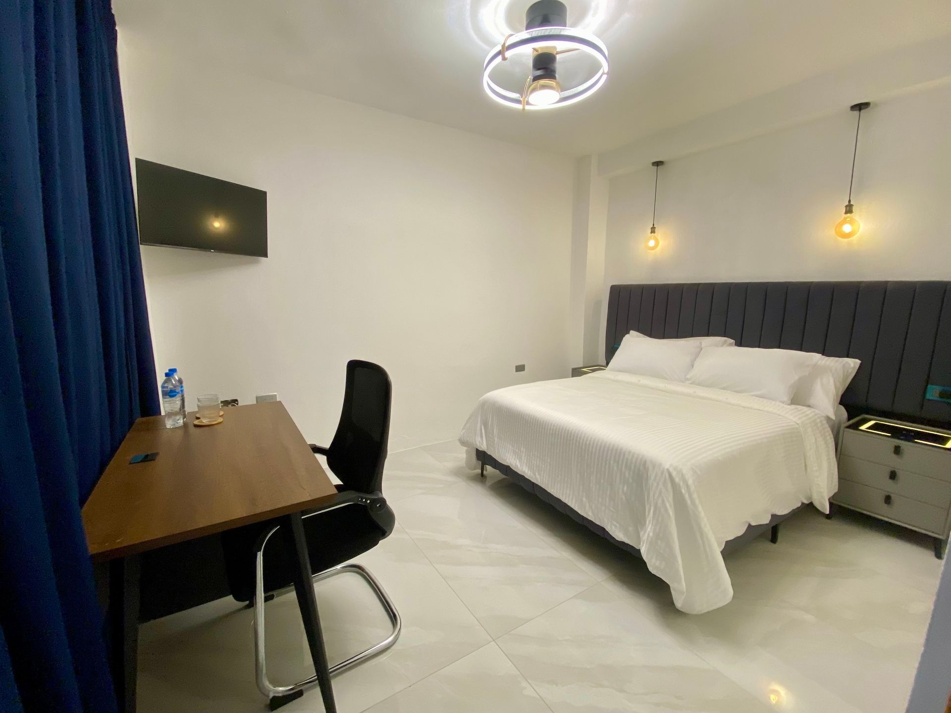 Bedroom with bed, desk, TV, and decorative lighting. White and blue color scheme.