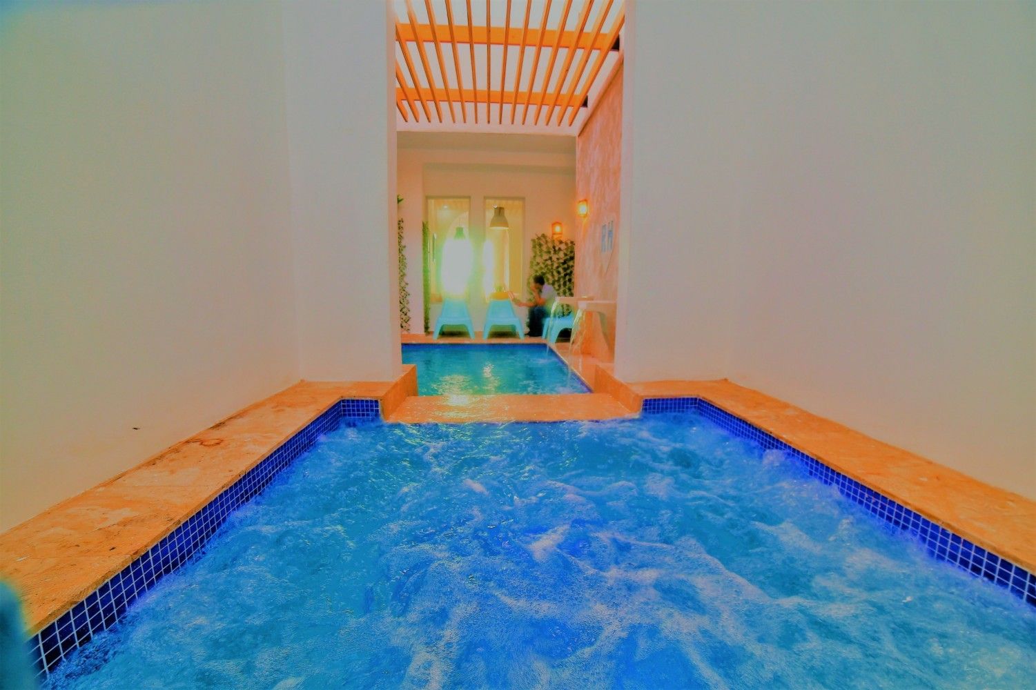 Indoor pool with blue water and tiled edges, leading to another pool and window.