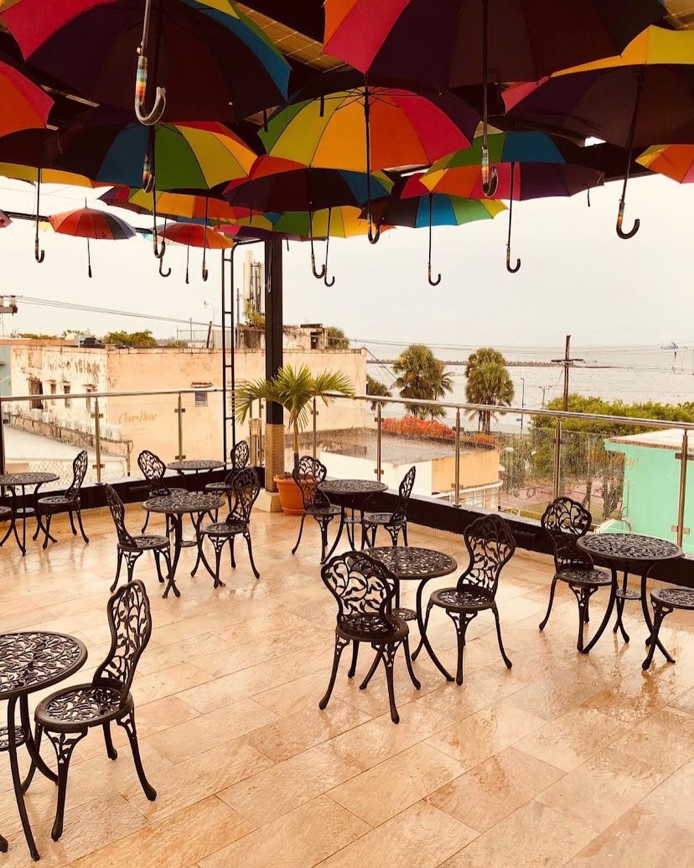 Outdoor cafe with black tables and chairs, under a ceiling of colorful umbrellas.