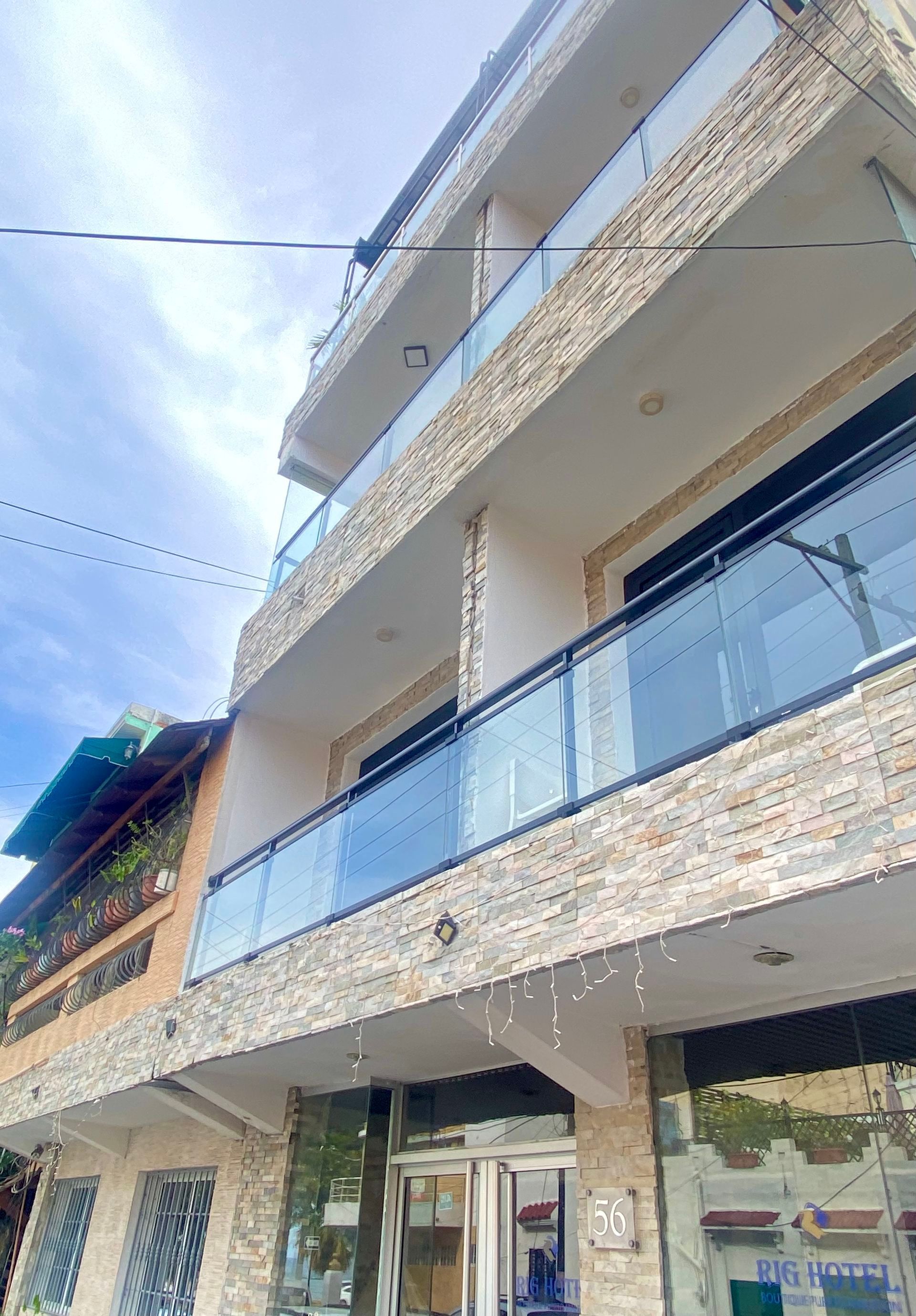 Multi-story building with stone facade and glass balconies under a cloudy sky.