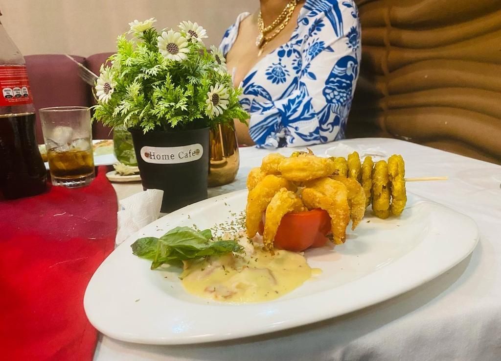A plate with fried food, a tomato, and sauce is in front of a person in a blue and white top.