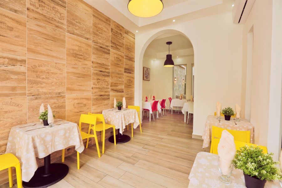 Restaurant interior with yellow chairs, tables with white tablecloths, and an arched doorway.