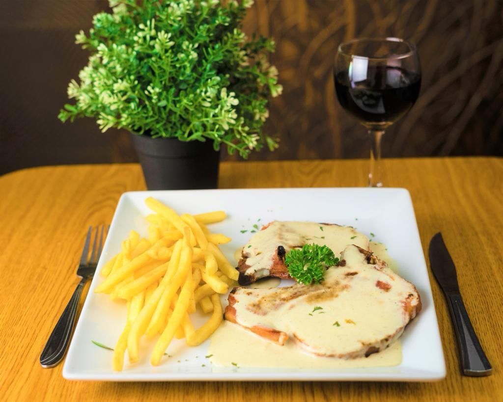 Steak with sauce, fries, and wine on a table, with a potted plant in the background.