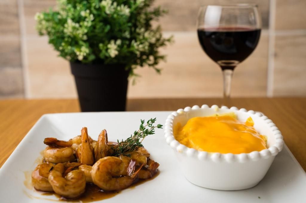 Plate of shrimp with orange mash, a glass of red wine, and a potted plant.