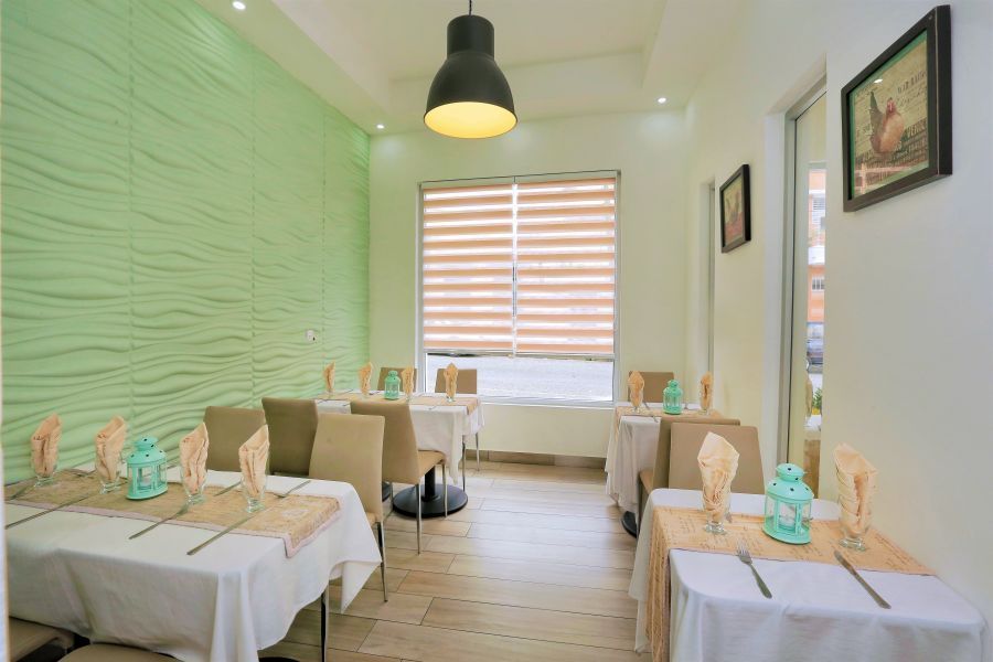 Restaurant interior with white-covered tables, beige chairs, and decorative wall.