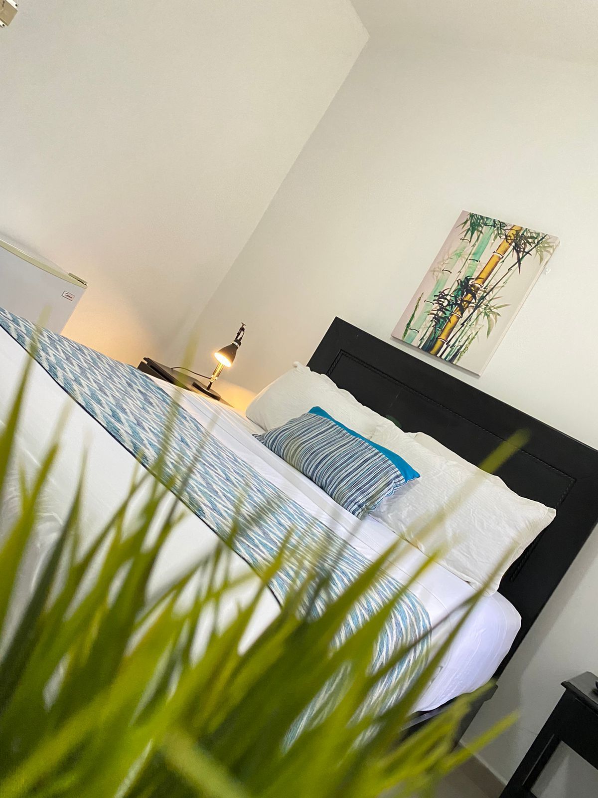Bedroom with black bed frame, white and blue bedding, bamboo art, and lamp.