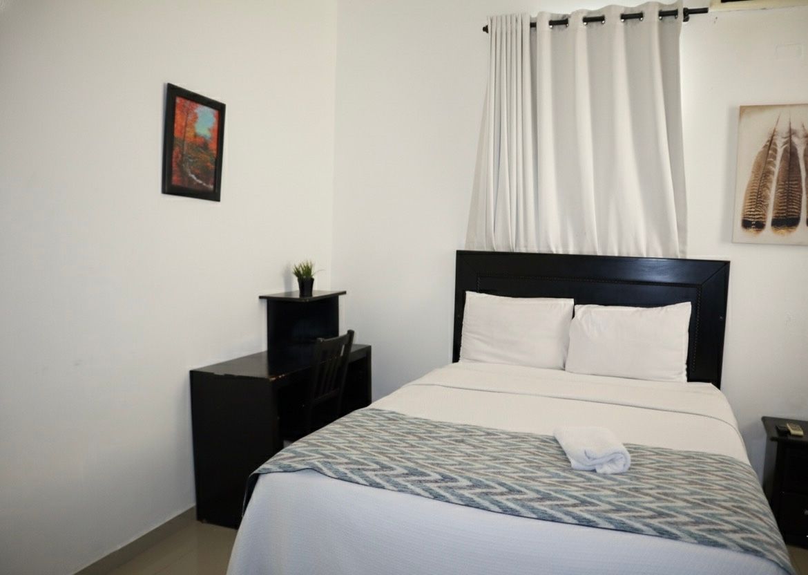 A minimalist bedroom with a bed, desk, artwork, and white curtains.