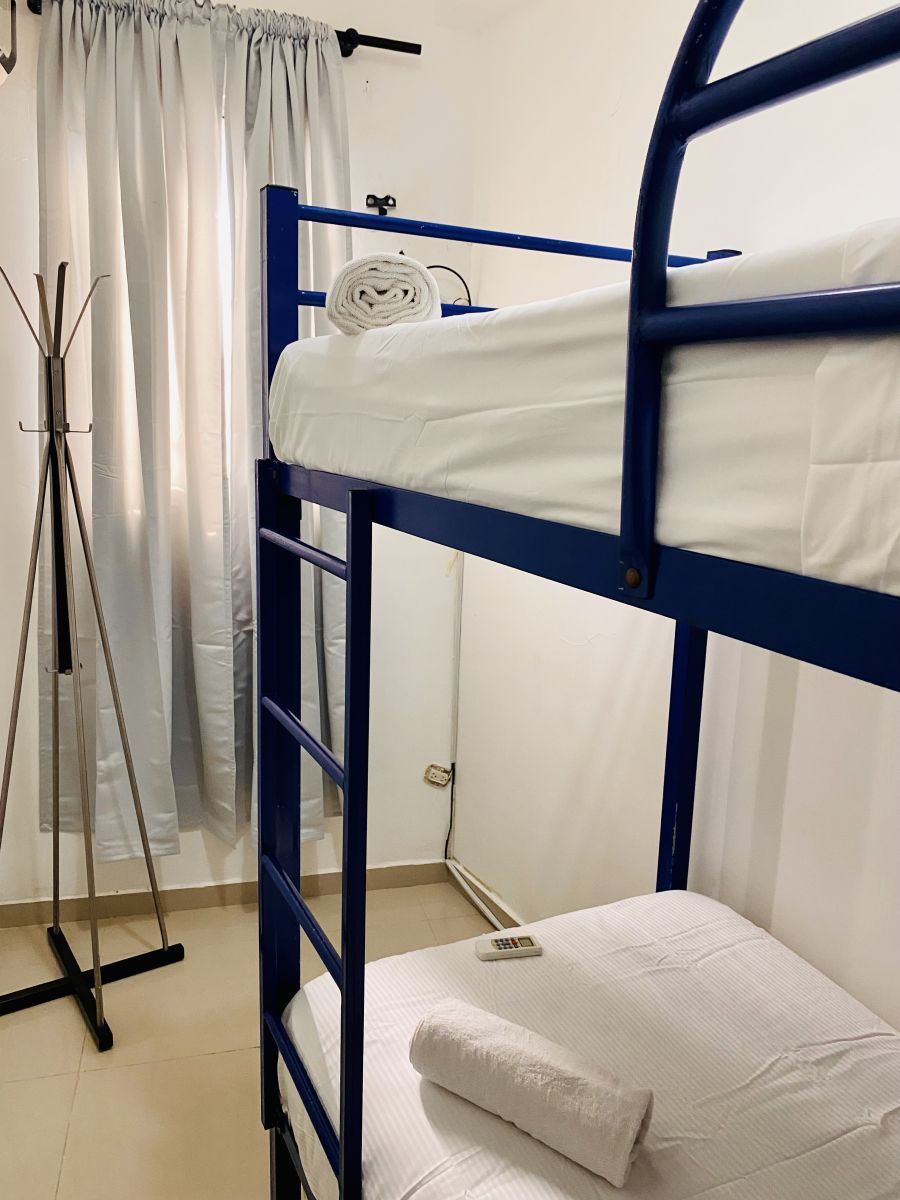 Blue bunk bed in a room with white sheets, curtains, and a coat rack.