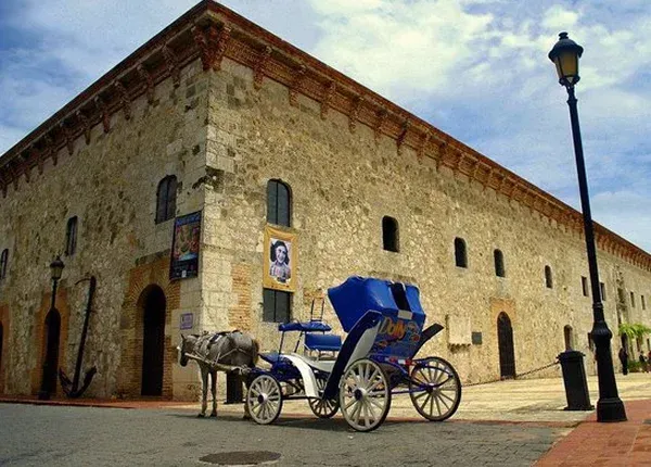 Stone building with arched windows, carriage with a blue top, and a street lamp.
