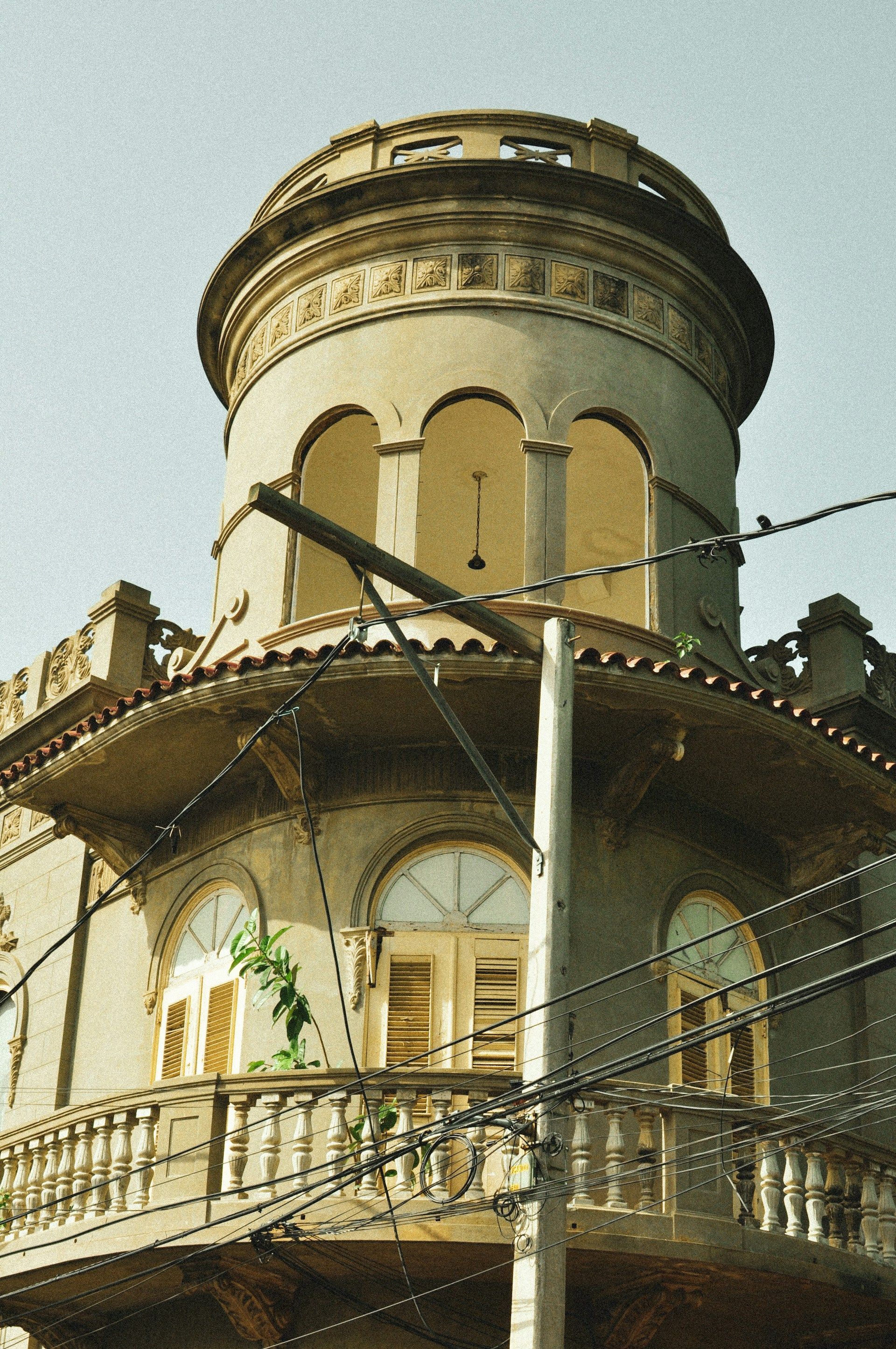Historic building with a cylindrical tower and arched windows, light-colored walls, and a balcony.