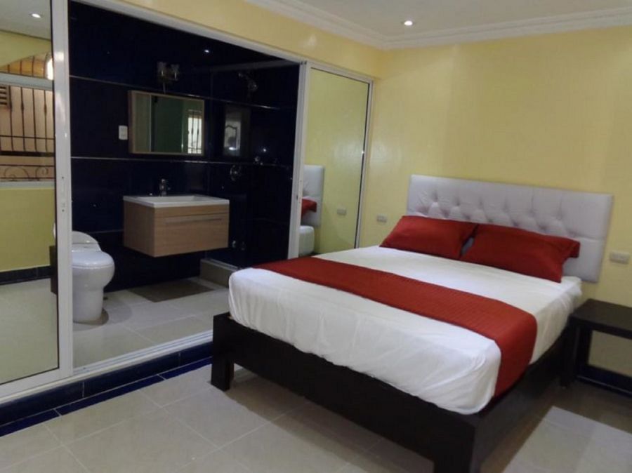 Bedroom with a bed, red accents, and a bathroom visible through a sliding glass door.