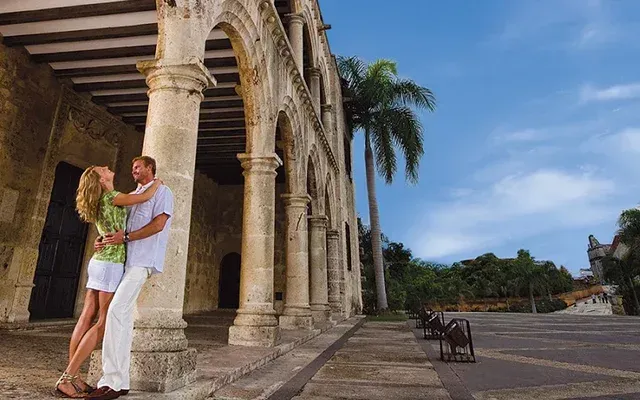 Couple embracing near stone columns, blue sky, palm tree in background.
