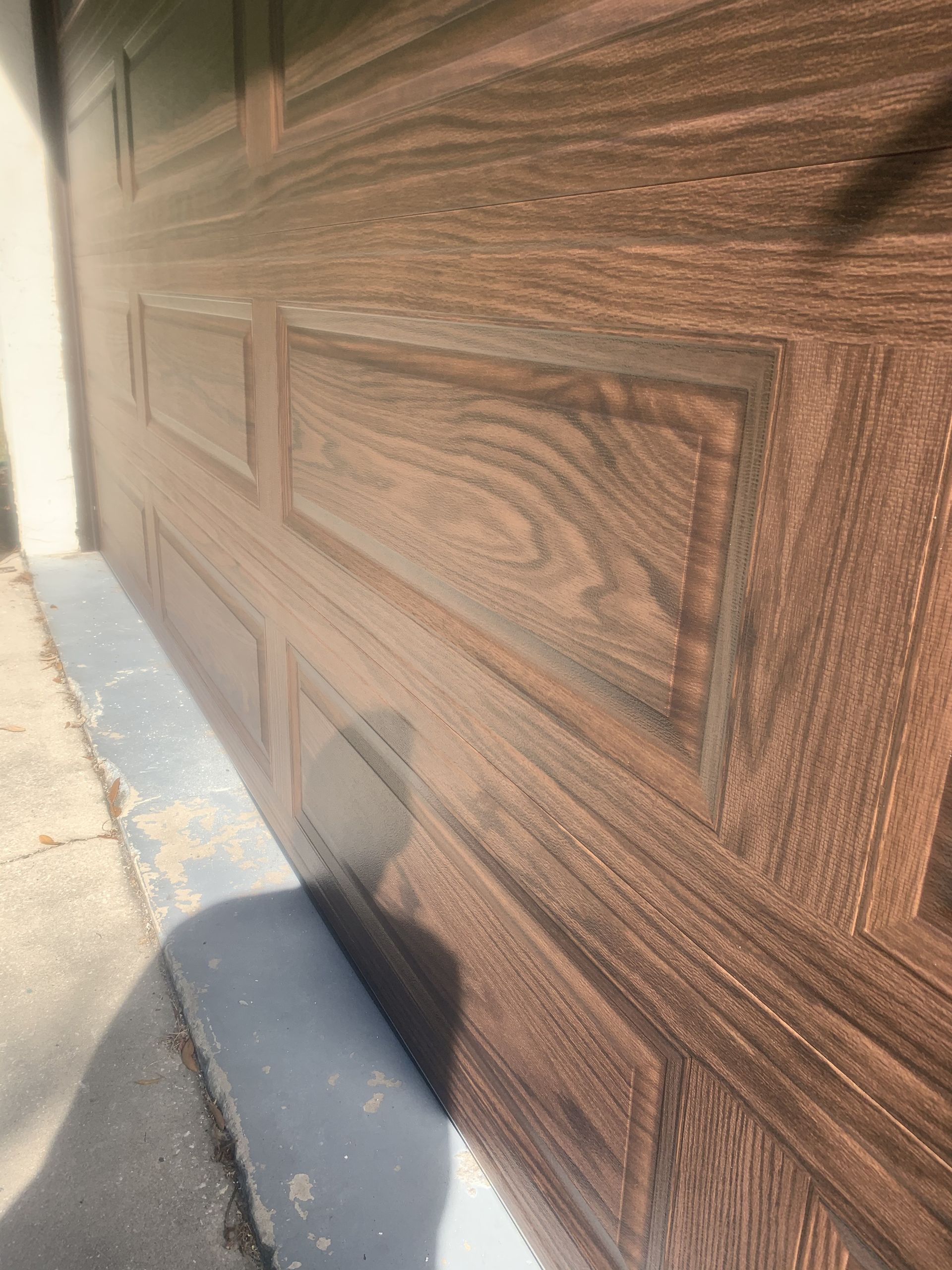 A close up of a wooden garage door with a shadow on the ground.
