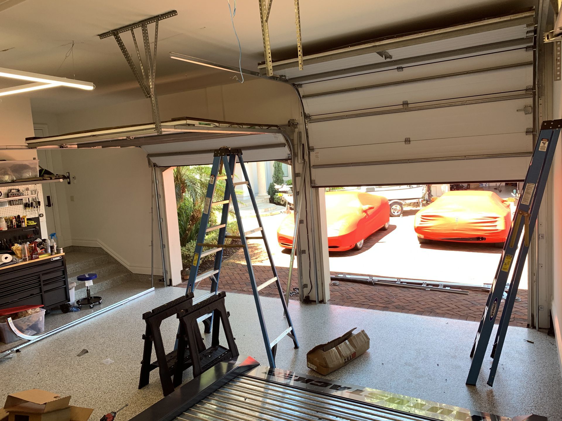 A garage door is open and a ladder is hanging from the ceiling.