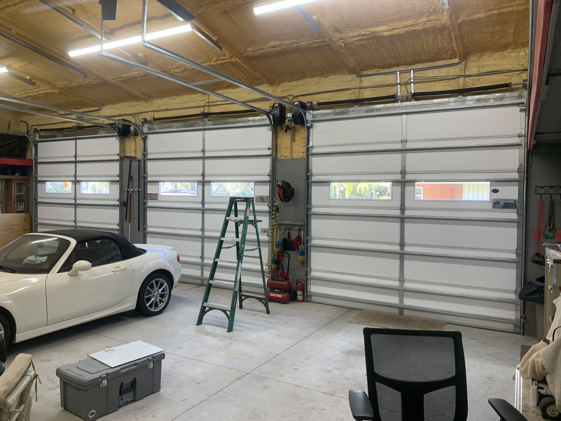 A white car is parked in a garage next to a ladder.