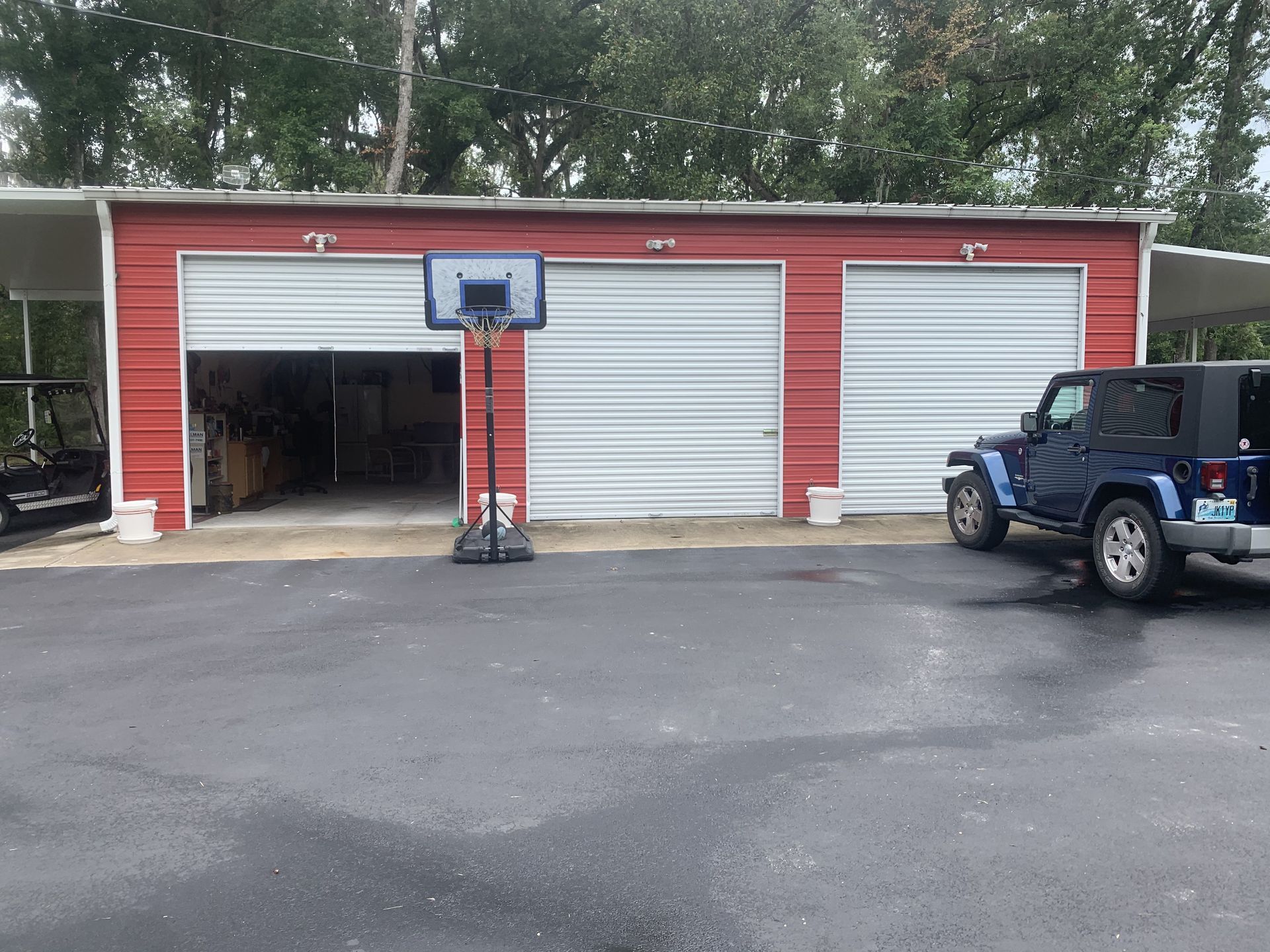 A jeep is parked in front of a garage with a basketball hoop.