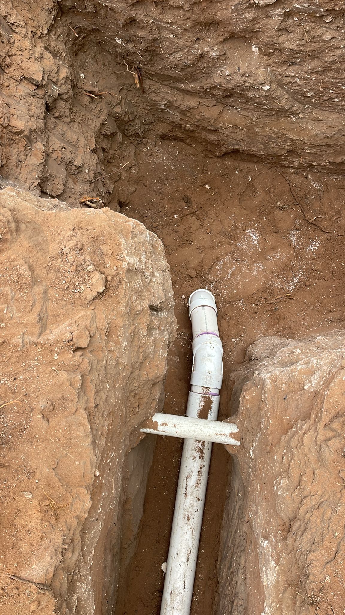 A white pipe is laying in the dirt in a hole.