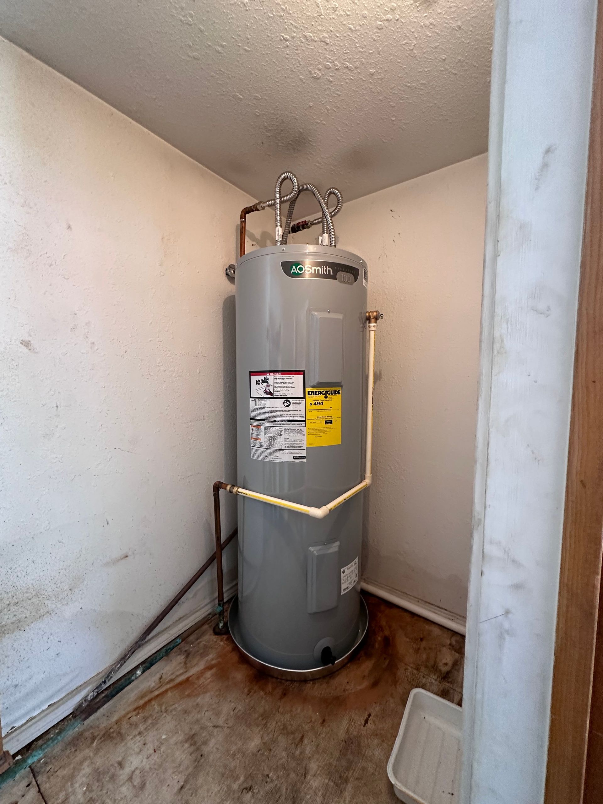 A water heater is sitting in a dirty room next to a wall.