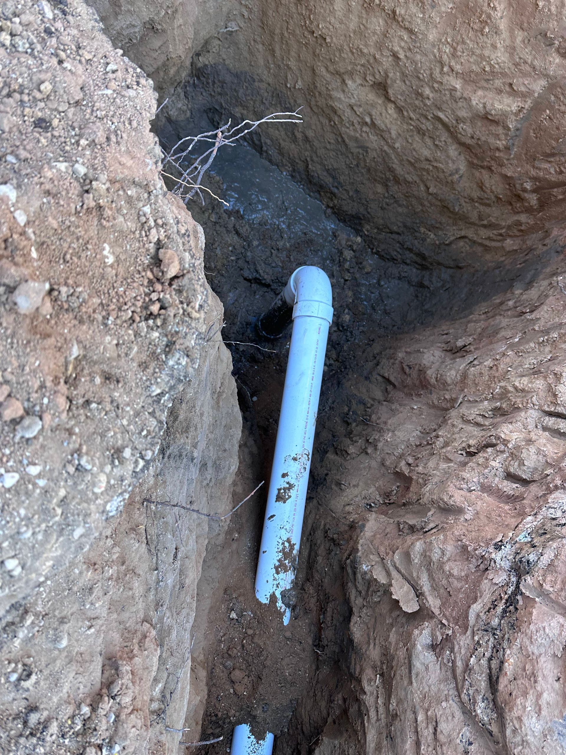 A white pipe is laying in the dirt in a hole