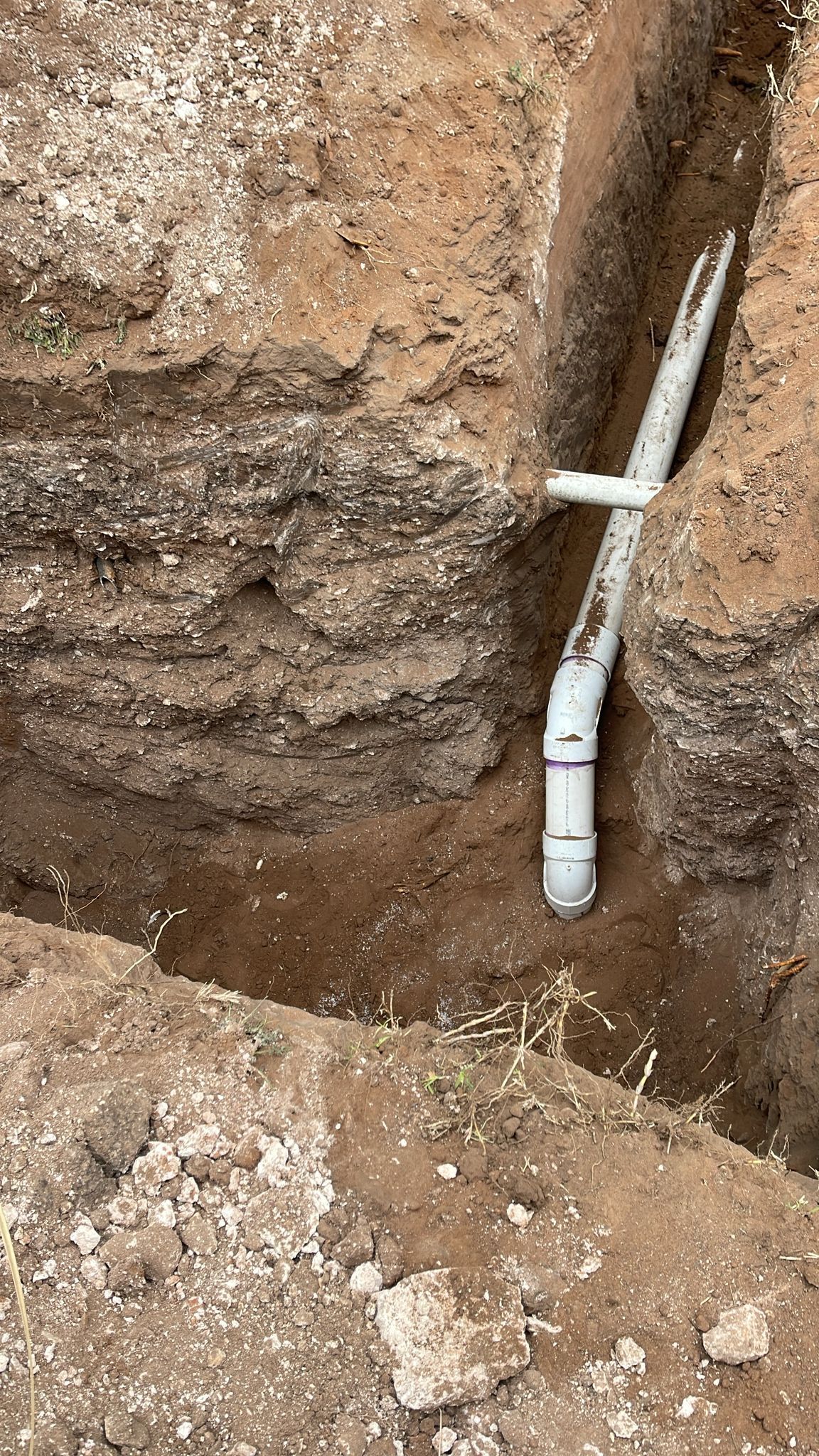 A white pipe is laying in the dirt in a hole.
