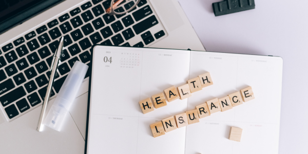 Scrabble tiles spelling health insurance on a planner beside a laptop, symbolizing Medicare vs private insurance decisions