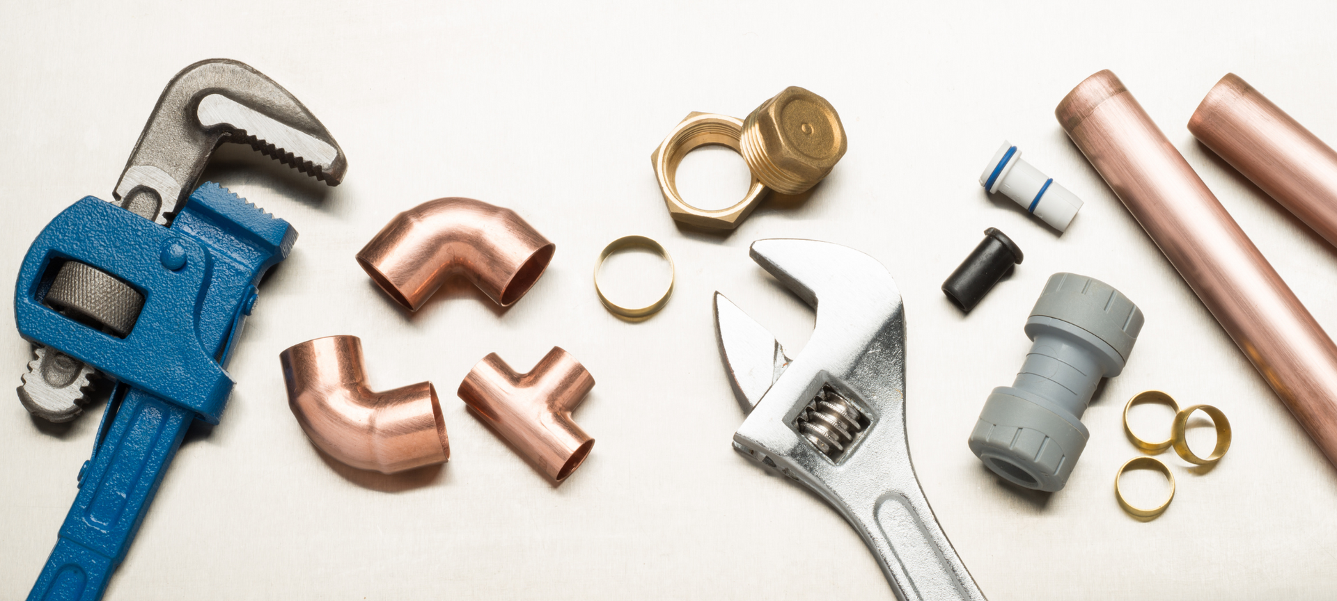 Plumbing tools and copper pipes arranged on a light background.